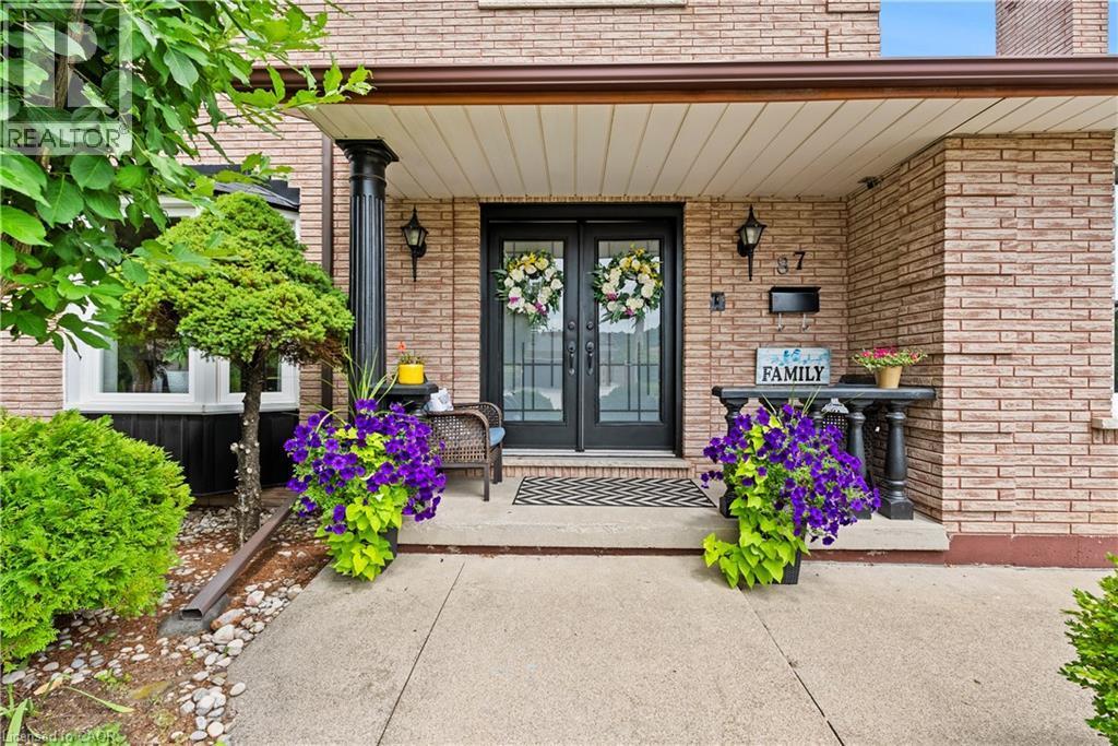Brick exterior with a covered porch featuring black columns, double entry doors with decorative glass, and exterior lighting fixtures - 87 Monte Drive, Hamilton, ON - Outdoor With Deck Patio Veranda