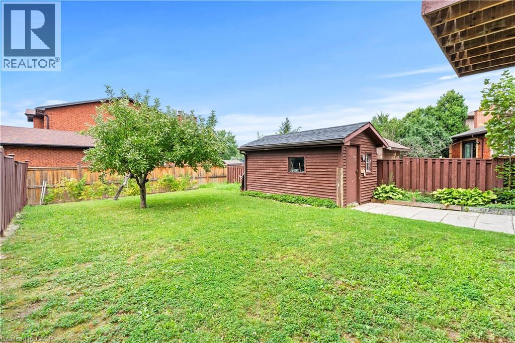 Expansive grassy yard with a mature tree, a detached storage shed, a paved pathway, and privacy fencing - 87 Monte Drive, Hamilton, ON - Outdoor
