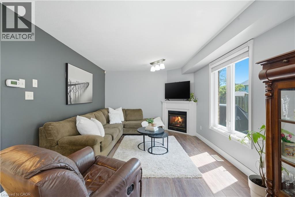 Living area featuring wood-finish flooring, a corner fireplace with a white mantel, and a large window with white trim - 784 Butternut Avenue, Waterloo, ON - Indoor Photo Showing Living Room With Fireplace