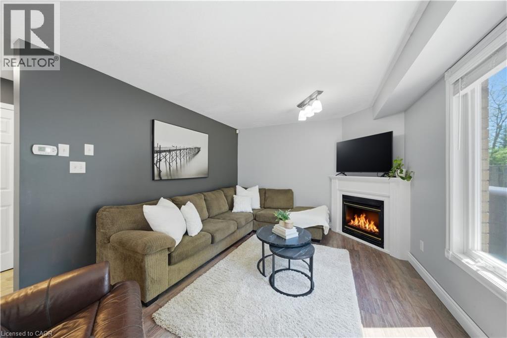 Living area featuring wood-finish flooring, a white trim window, and a corner fireplace with a white mantel - 784 Butternut Avenue, Waterloo, ON - Indoor Photo Showing Living Room With Fireplace