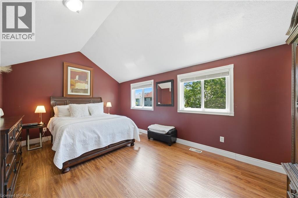Vaulted ceiling with a flush-mount light fixture, two windows with white trim, wood-finish flooring, and a deep red accent wall - 784 Butternut Avenue, Waterloo, ON - Indoor Photo Showing Bedroom