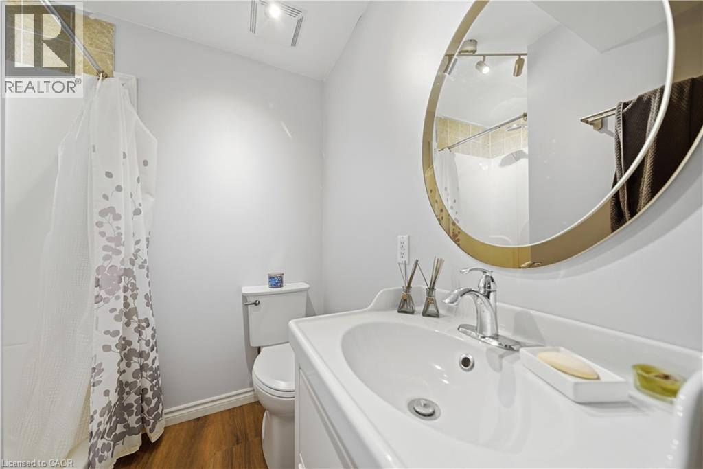 Bathroom with wood-finish flooring, a white vanity with integrated sink, and a circular mirror with a gold-toned frame - 784 Butternut Avenue, Waterloo, ON - Indoor Photo Showing Bathroom