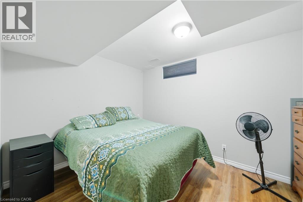 Recessed ceiling light fixture illuminating a room with wood-finish flooring, a white wall, and a horizontal window with a dark blind - 784 Butternut Avenue, Waterloo, ON - Indoor Photo Showing Bedroom