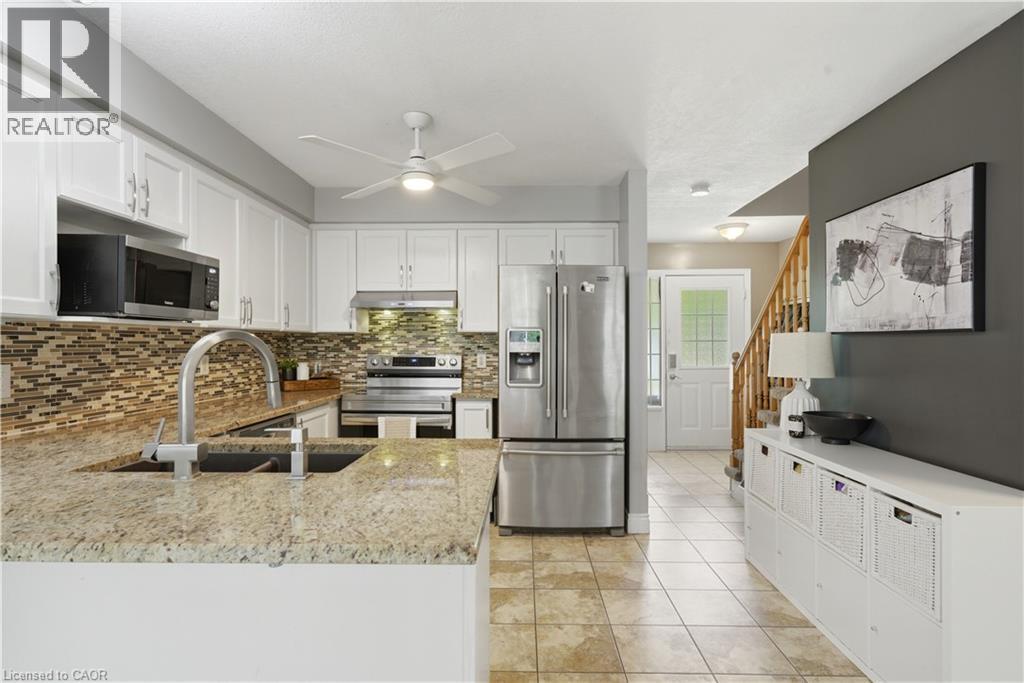 Kitchen featuring granite countertops, a double basin sink with gooseneck faucet, full-height tile backsplash, white cabinetry, and stainless steel appliances - 784 Butternut Avenue, Waterloo, ON - Indoor Photo Showing Kitchen With Double Sink With Upgraded Kitchen