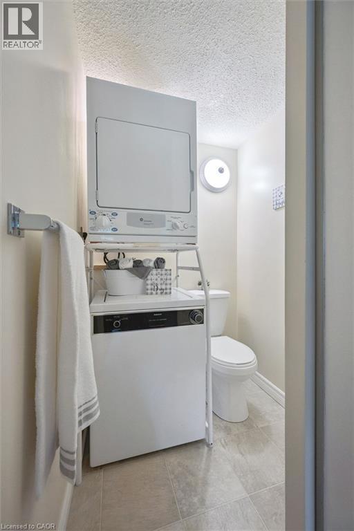 Stackable washer and dryer, tile flooring, wall-mounted towel bar, and a toilet - 6 Walton Avenue Unit# 107, Kitchener, ON - Indoor Photo Showing Bathroom