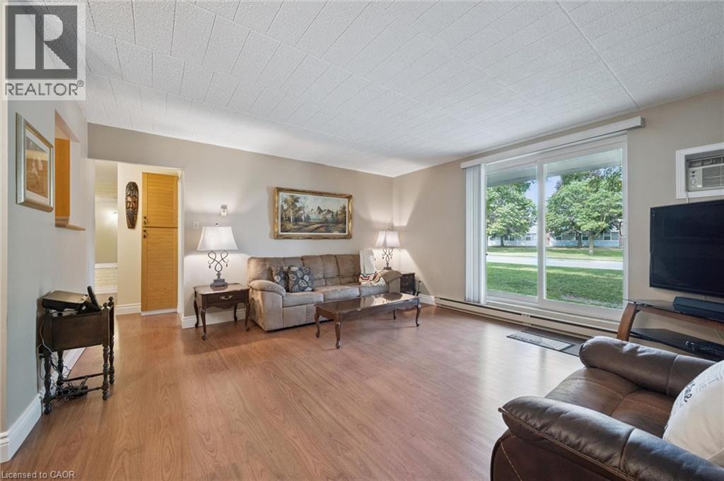 Wood-finish flooring throughout, sliding glass door with blinds, and built-in vertical cabinetry - 6 Walton Avenue Unit# 107, Kitchener, ON - Indoor Photo Showing Living Room