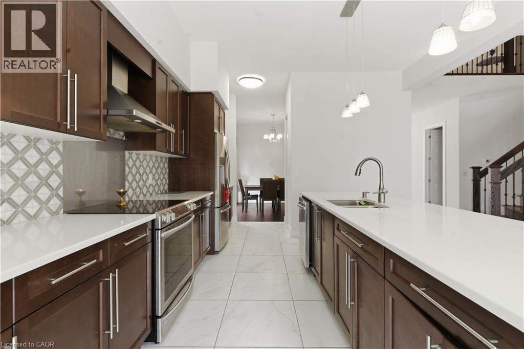 Chef's kitchen featuring rich wood cabinetry with stainless steel appliances, white quartz countertops, geometric tile backsplash, recessed and pendant lighting, and an oversized island with seating s - 2000 Maddex Way, London, ON - Indoor Photo Showing Kitchen With Double Sink With Upgraded Kitchen