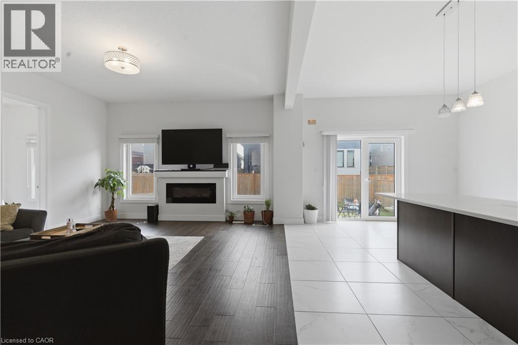 Open-concept living space featuring dark wood-finish flooring, a linear gas fireplace with white surround and built-in cabinetry, a wall-mounted flat-screen television, recessed and pendant lighting, - 2000 Maddex Way, London, ON - Indoor Photo Showing Living Room
