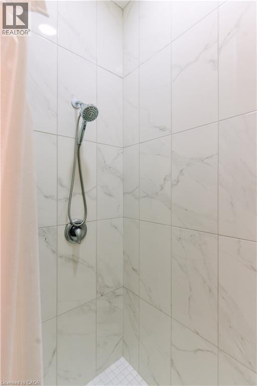 Spa-inspired shower enclosure featuring large-format tile walls with natural stone veining, dual showerheads with adjustable spray patterns, and a built-in niche for convenient storage - 2000 Maddex Way, London, ON - Indoor Photo Showing Bathroom