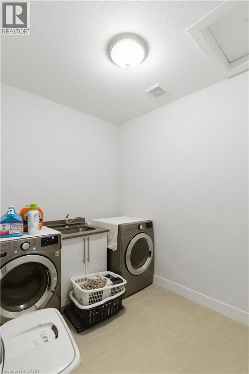 Dedicated laundry room featuring side-by-side front-load washers and dryers, ample counter space with cabinetry for storage, recessed ceiling lighting, and light wood-finish flooring throughout - 2000 Maddex Way, London, ON - Indoor Photo Showing Laundry Room