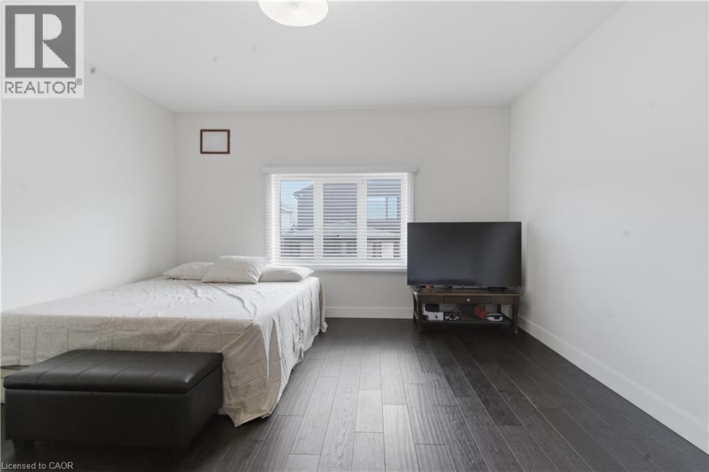 Bright bedroom offering dark wood-finish flooring, a bed with neutral linens, and a black storage bench - 2000 Maddex Way, London, ON - Indoor Photo Showing Bedroom
