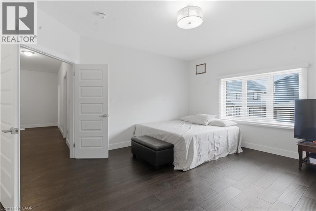 Spacious bedroom featuring dark wood-finish flooring, abundant natural light from large multi-pane windows with plantation shutters, and an ensuite walk-in closet - 2000 Maddex Way, London, ON - Indoor Photo Showing Bedroom