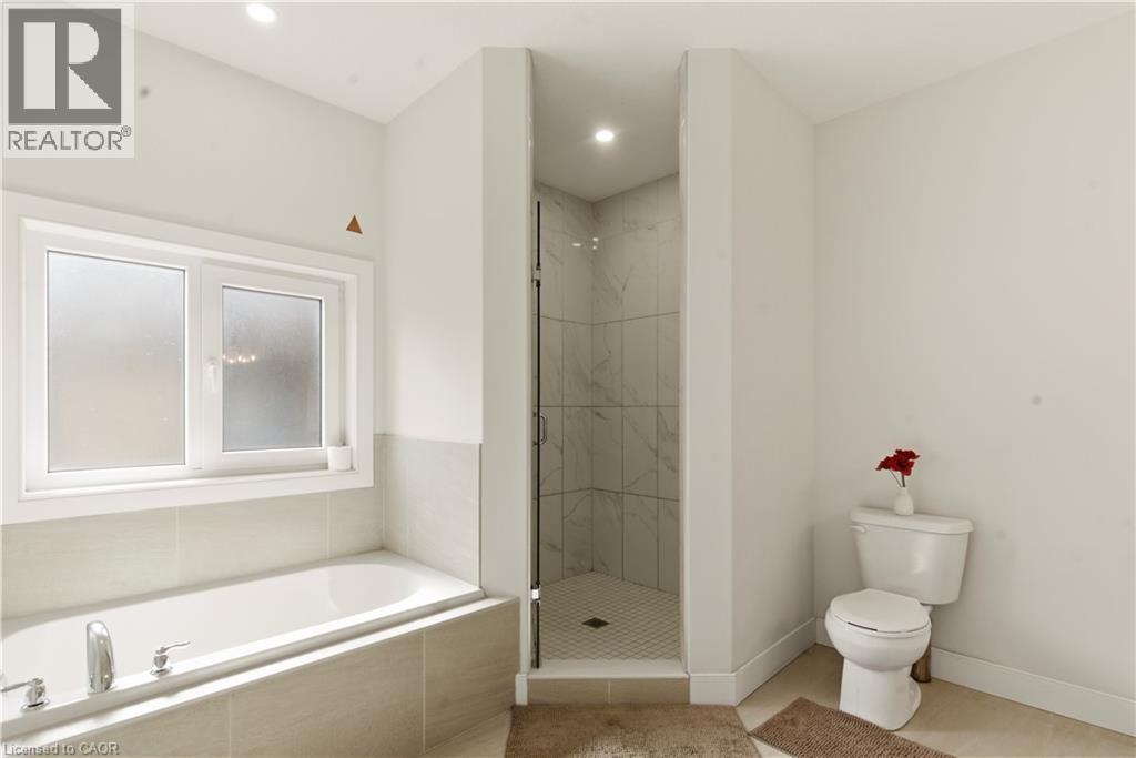 Modern primary bathroom featuring a soaking tub with tile surround, a corner walk-in shower with glass enclosure and tile walls, dual vanity sink, and wood-finish flooring - 2000 Maddex Way, London, ON - Indoor Photo Showing Bathroom