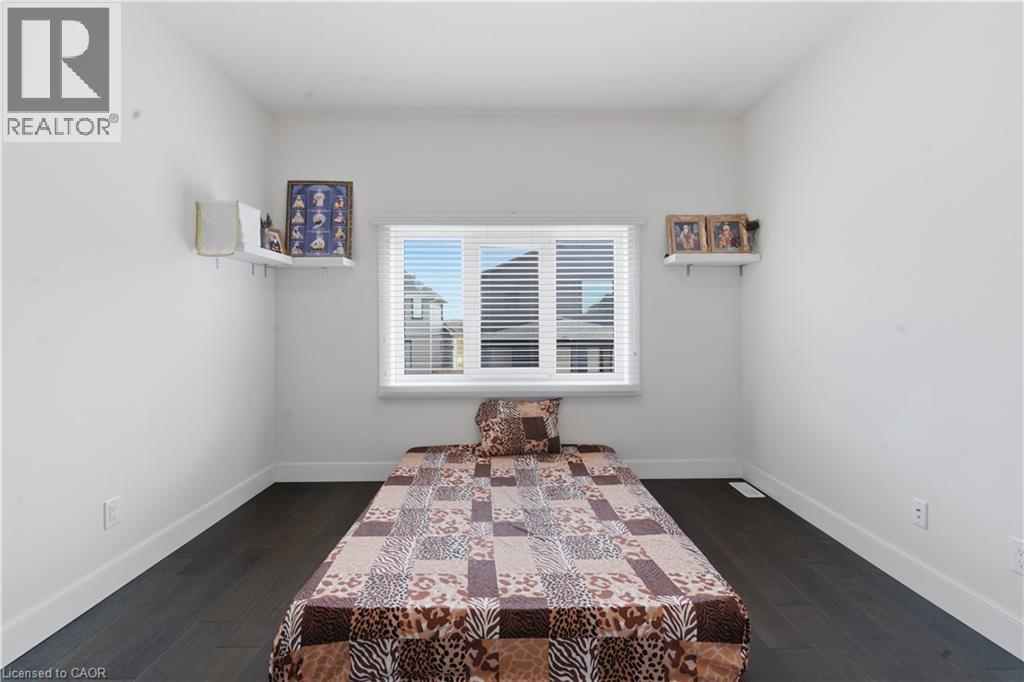Bright bedroom featuring dark wood-finish flooring, white walls, and a large multi-pane window with horizontal blinds allowing abundant natural light - 2000 Maddex Way, London, ON - Indoor