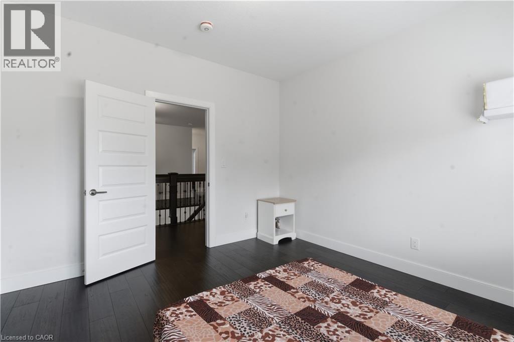 Bright secondary bedroom featuring pristine white walls, dark wood-finish flooring, and clean-lined white panel door - 2000 Maddex Way, London, ON - Indoor