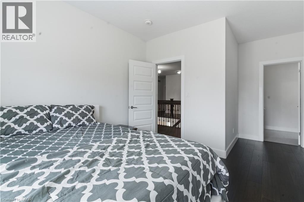 Spacious bedroom featuring dark wood-finish flooring, geometric patterned bedding, and abundant natural light from multiple windows - 2000 Maddex Way, London, ON - Indoor Photo Showing Bedroom