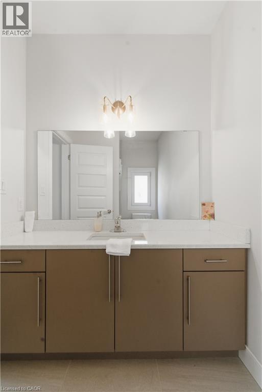 Spa-inspired bathroom vanity featuring warm wood-finish cabinetry with ample storage, a white quartz countertop, and an expansive framed mirror - 2000 Maddex Way, London, ON - Indoor