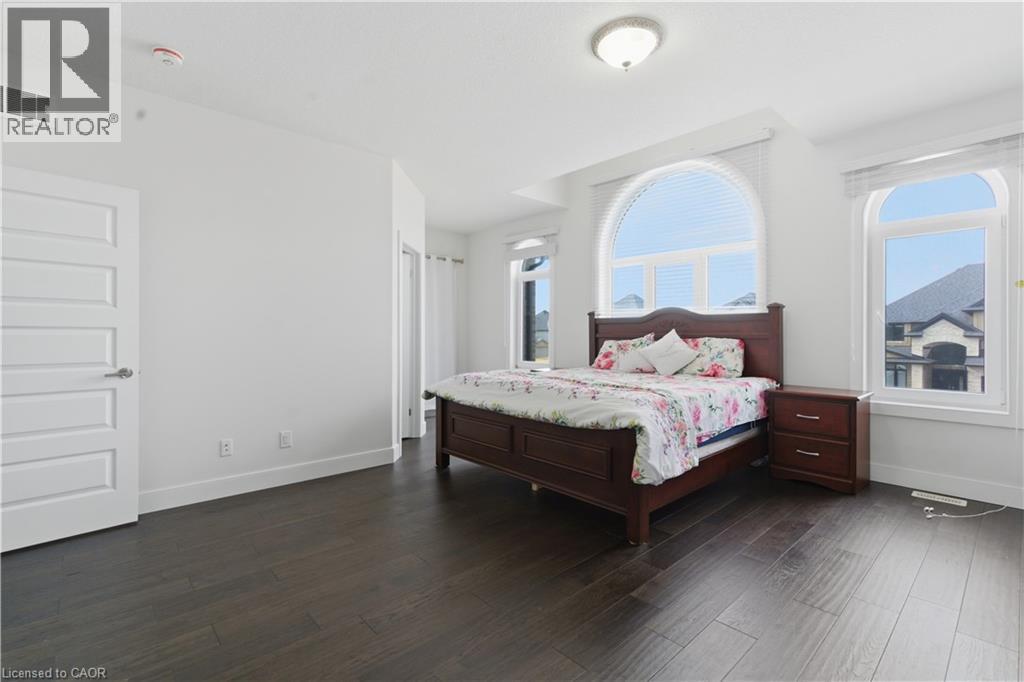 Dark wood-finish flooring, white paneled interior door, arched windows, recessed lighting, and a semi-flush mount ceiling fixture - 2000 Maddex Way, London, ON - Indoor Photo Showing Bedroom