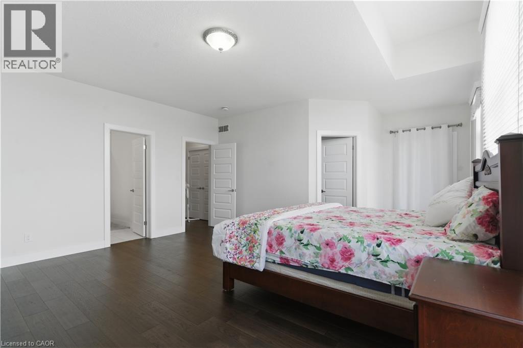 Spacious primary bedroom featuring dark wood-finish flooring, multiple closet entries with louvered doors, recessed ceiling lighting, and abundant natural light from windows along the perimeter walls - 2000 Maddex Way, London, ON - Indoor Photo Showing Bedroom