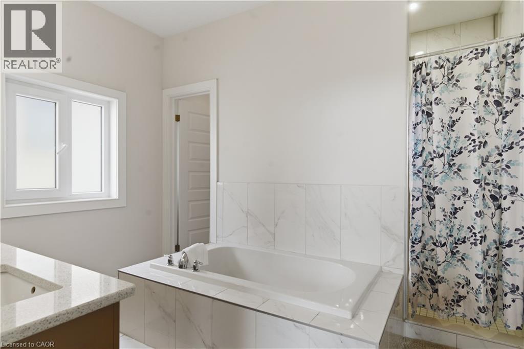 Built-in soaking tub, large vanity with integrated sink and stone-look countertop, tile surround, and an enclosed shower - 2000 Maddex Way, London, ON - Indoor Photo Showing Bathroom