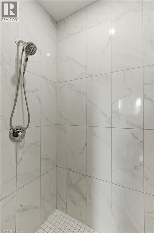 Spa-inspired shower featuring large-format marble-look tile walls with coordinating grout lines, dual showerheads with handheld spray attachment, chrome fixtures, and mosaic tile flooring - 2000 Maddex Way, London, ON - Indoor Photo Showing Bathroom
