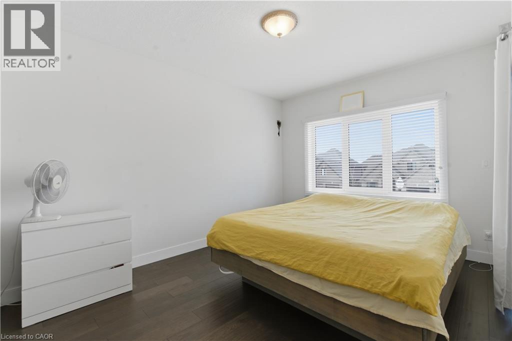 Dark wood-finish flooring, white walls, and a large window with horizontal blinds - 2000 Maddex Way, London, ON - Indoor Photo Showing Bedroom