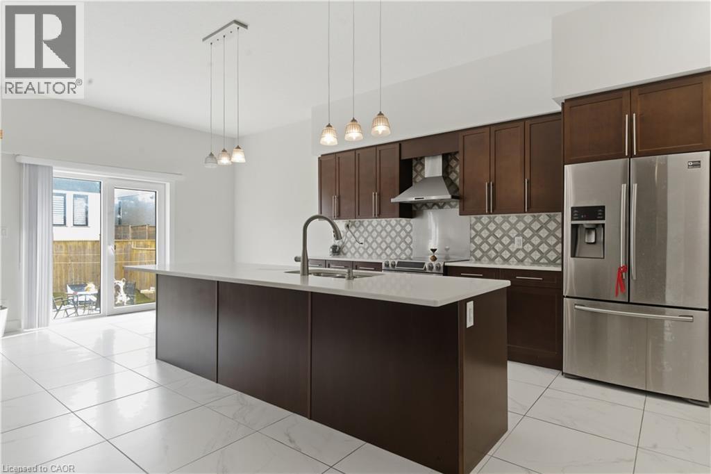 White tile flooring, kitchen island with a built-in sink, stainless steel appliances, dark wood-finish cabinetry, and sliding glass door - 2000 Maddex Way, London, ON - Indoor Photo Showing Kitchen With Double Sink With Upgraded Kitchen