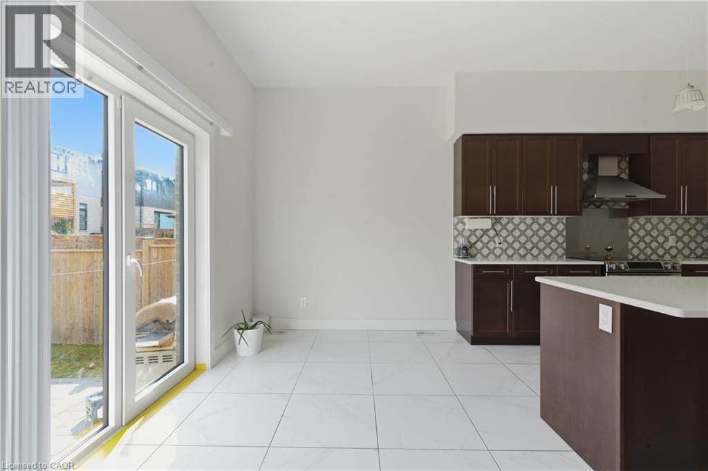 Modern kitchen featuring dark wood cabinetry with stainless steel hardware, a decorative tile backsplash, and a curved island with seating - 2000 Maddex Way, London, ON - Indoor Photo Showing Kitchen