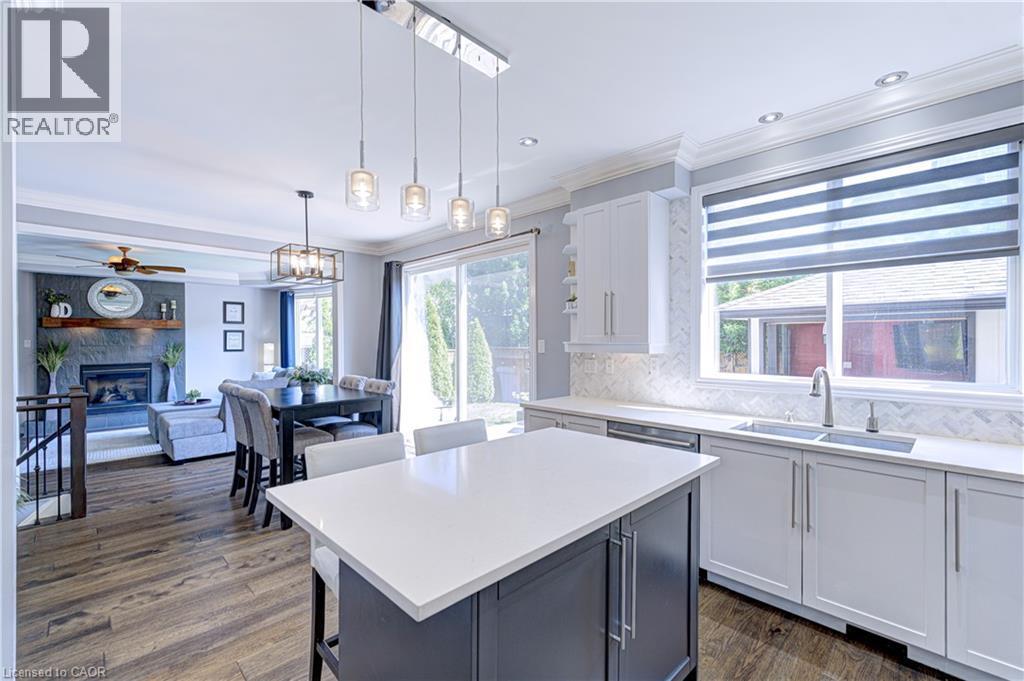 Open-concept kitchen featuring a large island with white countertop, white shaker-style cabinetry, and herringbone tile backsplash - 1406 Marshall Crescent, Milton, ON - Indoor Photo Showing Kitchen With Fireplace