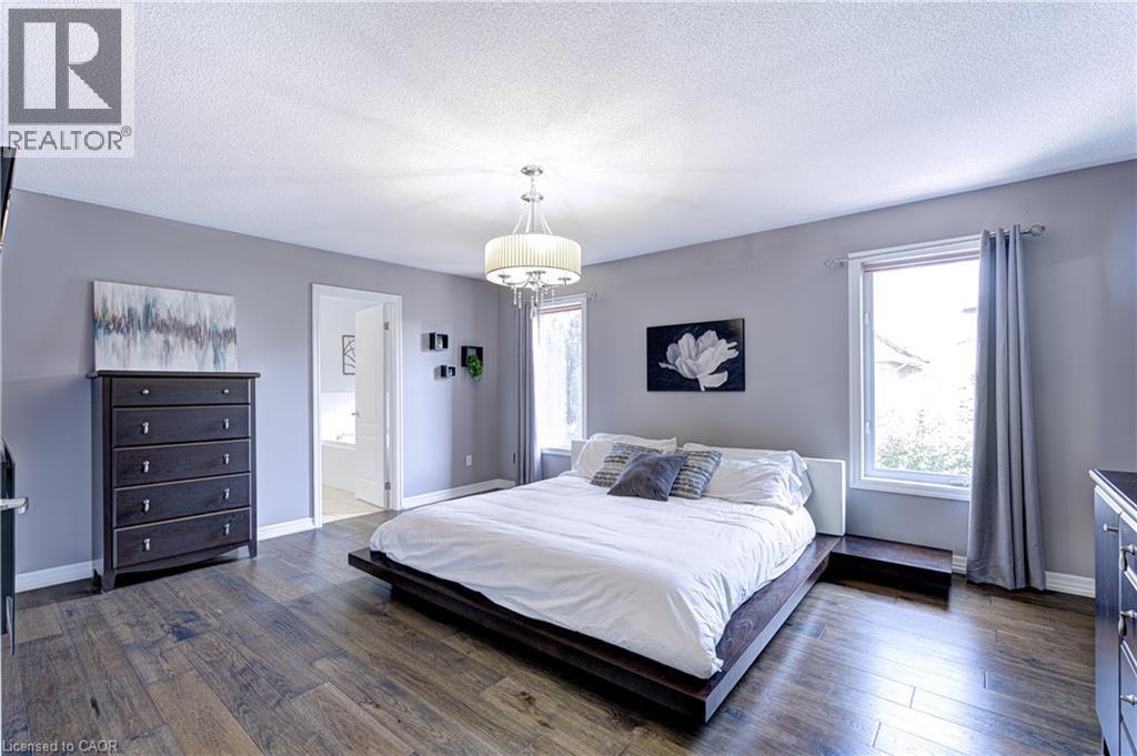 Spacious room featuring wide plank wood-finish flooring, a contemporary chandelier, two windows with white trim, and a doorway leading to an adjoining room - 1406 Marshall Crescent, Milton, ON - Indoor Photo Showing Bedroom