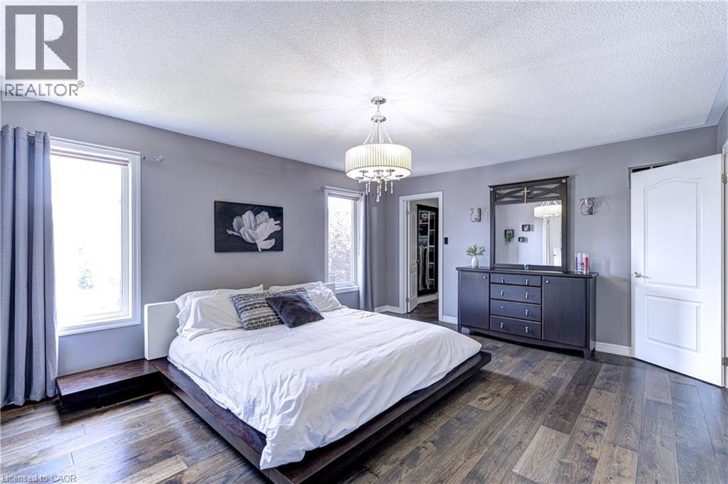 Spacious bedroom featuring wood-finish flooring, light gray walls, two windows, and a chandelier-style light fixture - 1406 Marshall Crescent, Milton, ON - Indoor Photo Showing Bedroom