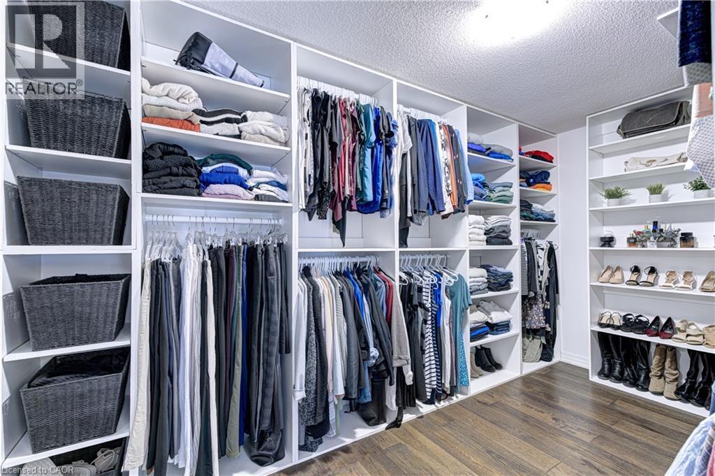 Custom walk-in closet featuring extensive built-in shelving, multiple hanging rods, dedicated shoe storage, wood-finish flooring, and recessed ceiling lighting - 1406 Marshall Crescent, Milton, ON - Indoor With Storage