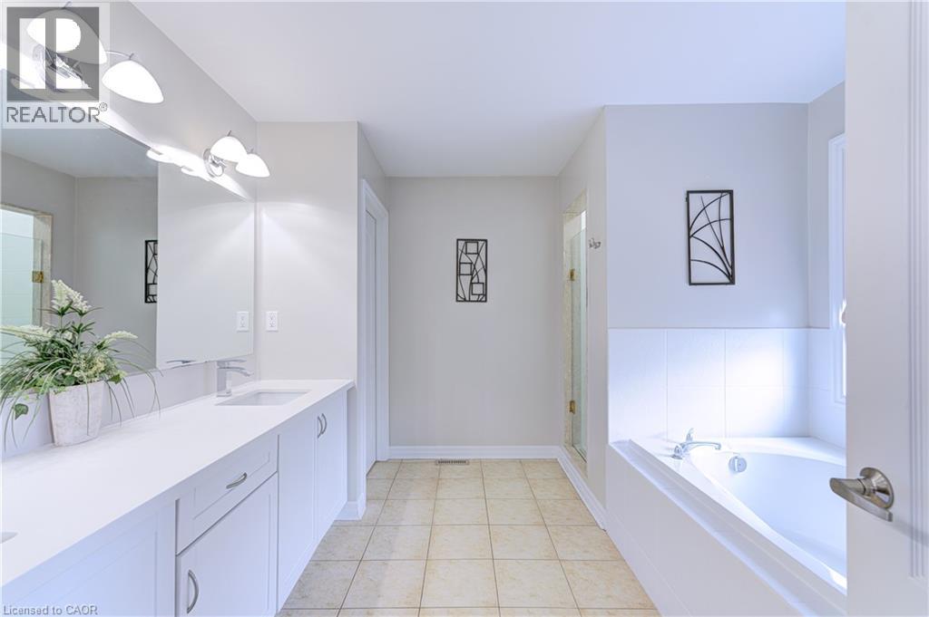 Bathroom featuring a dual vanity with white cabinetry and integrated sinks, a built-in bathtub with white tile surround, and tile flooring - 1406 Marshall Crescent, Milton, ON - Indoor Photo Showing Bathroom