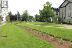 Landscaped green space featuring a paved walkway, mature trees, and planted garden beds -