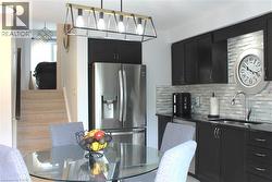 Modern kitchen featuring dark cabinetry, stainless steel appliances, a mosaic tile backsplash, and a sleek pendant light fixture -