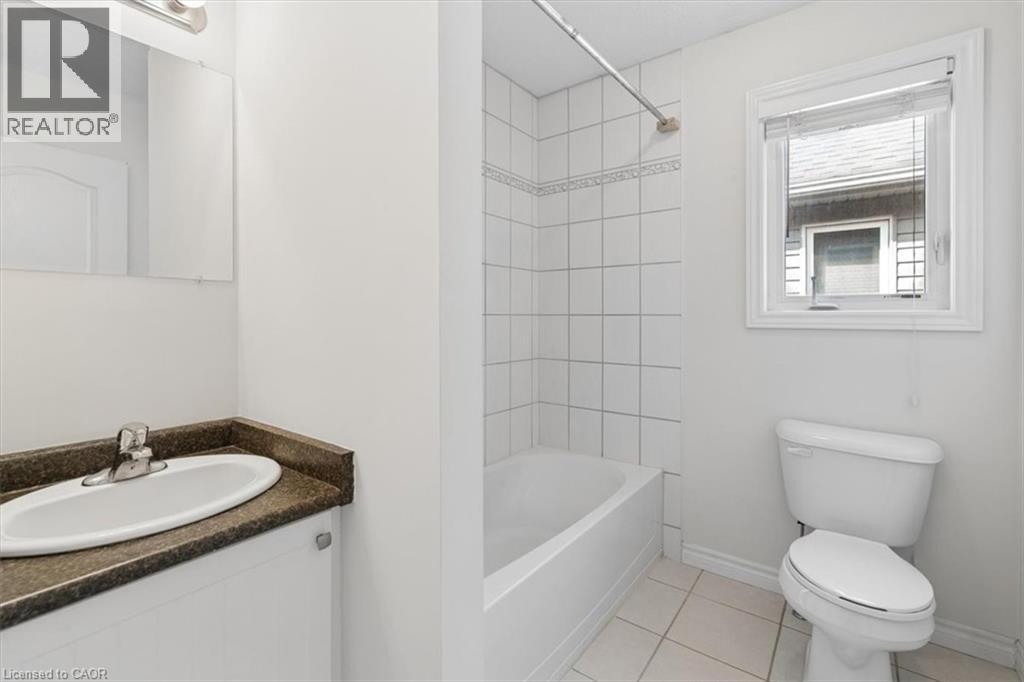 Bathroom featuring a vanity with an integrated sink, a full bathtub with tile surround, a toilet, a window with blinds, and tile flooring - 242 Moorlands Crescent, Kitchener, ON - Indoor Photo Showing Bathroom