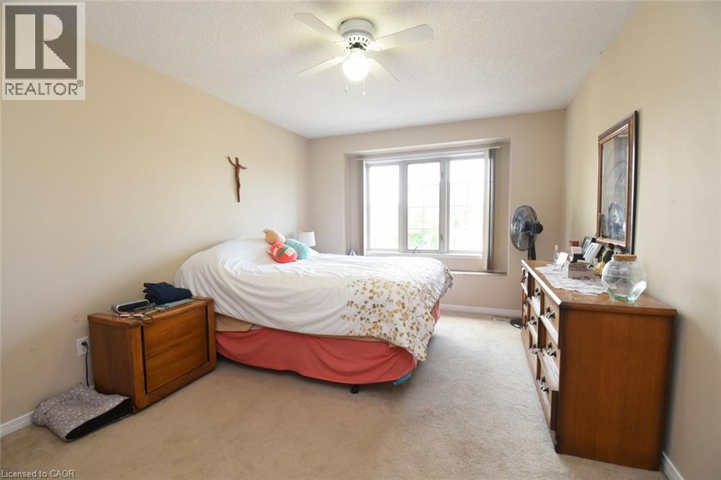 Spacious bedroom featuring neutral wall finishes, wall-mounted ceiling fan with integrated lighting, large multi-pane window with natural light, and wood-finish dresser and nightstand storage - 509 Southridge Drive, Hamilton, ON - Indoor Photo Showing Bedroom