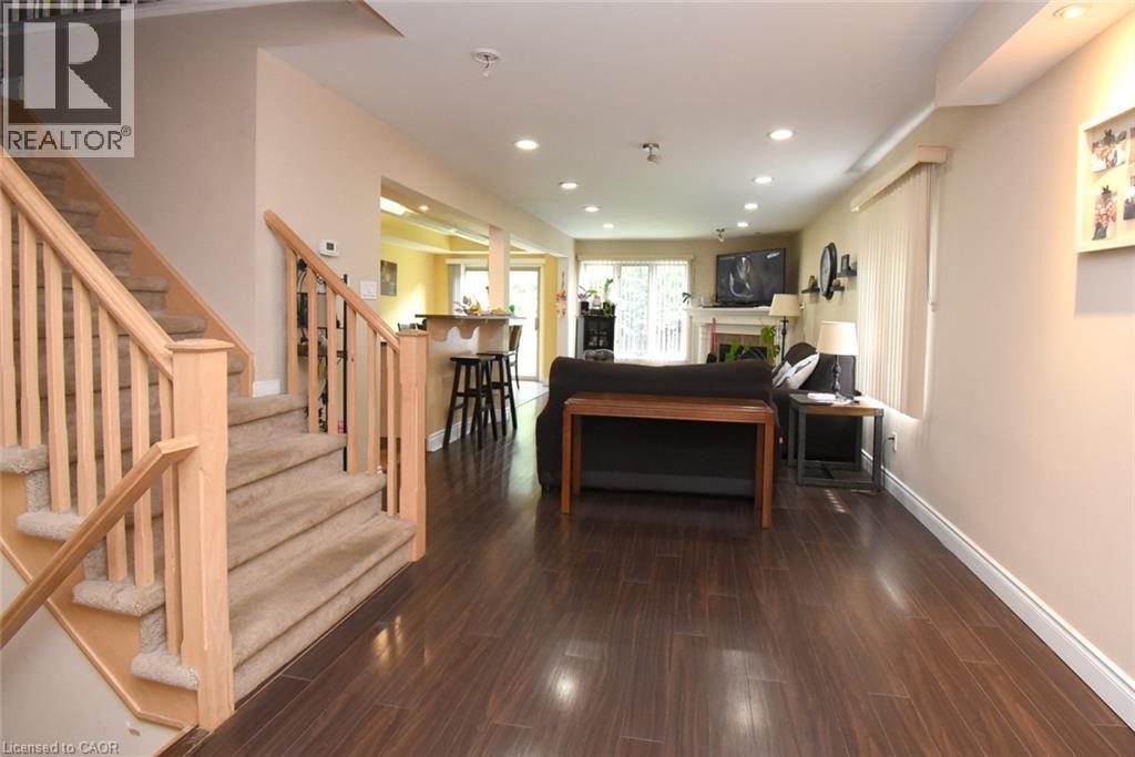Open-concept living space featuring dark wood-finish flooring throughout, a wooden staircase with turned balusters and natural wood railings, recessed ceiling lighting, and a kitchen area with black a - 509 Southridge Drive, Hamilton, ON - Indoor Photo Showing Other Room