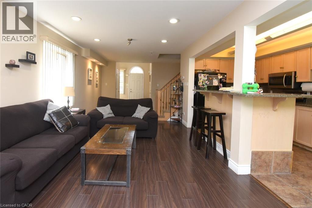 Open-concept living and kitchen area featuring dark wood-finish flooring throughout, a spacious black upholstered sectional sofa, wood coffee table, recessed ceiling lighting, and a kitchen with wood - 509 Southridge Drive, Hamilton, ON - Indoor Photo Showing Living Room