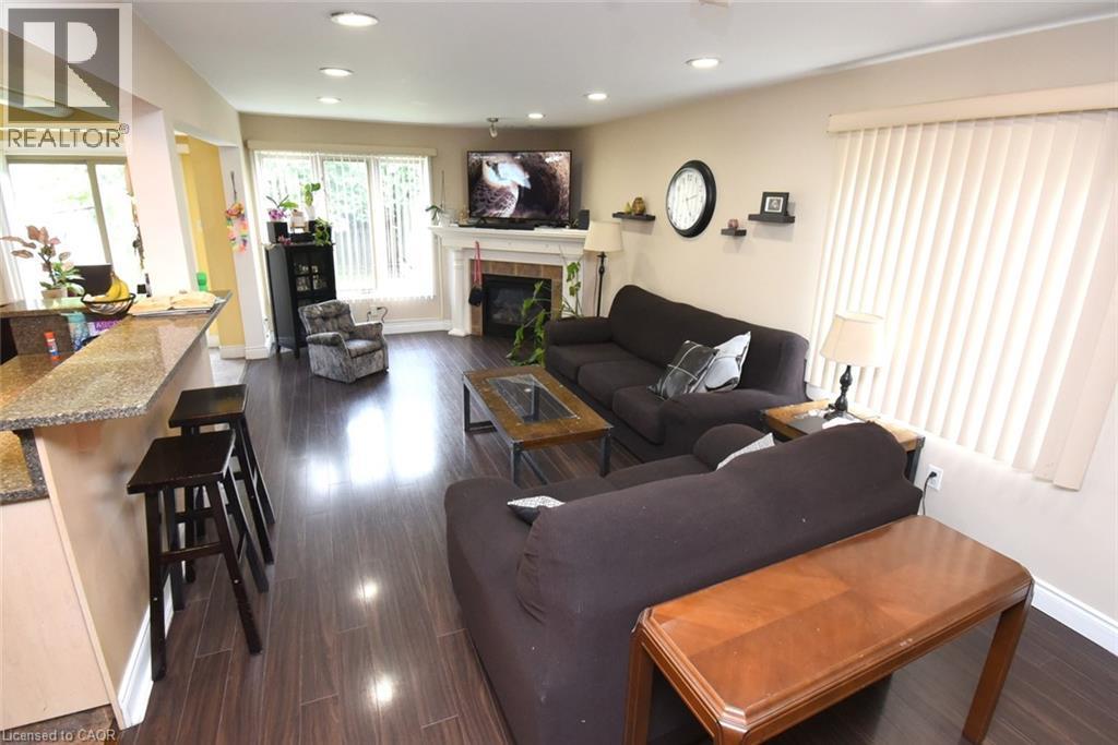 Open-concept living space featuring dark wood-finish flooring throughout, a fireplace with mantel display, recessed ceiling lighting, and a kitchen with granite countertops and island seating - 509 Southridge Drive, Hamilton, ON - Indoor Photo Showing Living Room With Fireplace