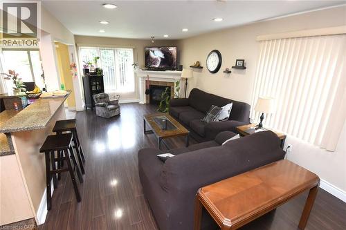 Open-concept living space featuring dark wood-finish flooring throughout, a fireplace with mantel display, recessed ceiling lighting, and a kitchen with granite countertops and island seating - 509 Southridge Drive, Hamilton, ON - Indoor Photo Showing Living Room With Fireplace