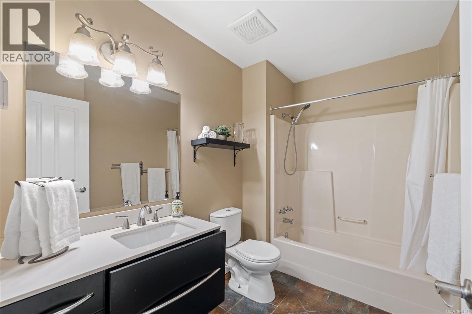 Master Bathroom featuring a single vanity with a white countertop, dark cabinetry, an integrated sink, and a combination shower/tub - 4105 Ross Rd, Nanaimo, BC - Indoor Photo Showing Bathroom