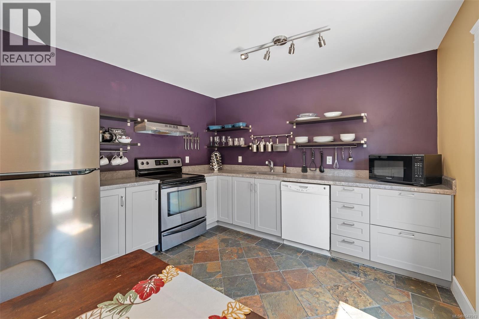 Stainless steel appliances, built-in shelving, stone tile flooring, and a breakfast bar with built-in seating - 4105 Ross Rd, Nanaimo, BC - Indoor Photo Showing Kitchen
