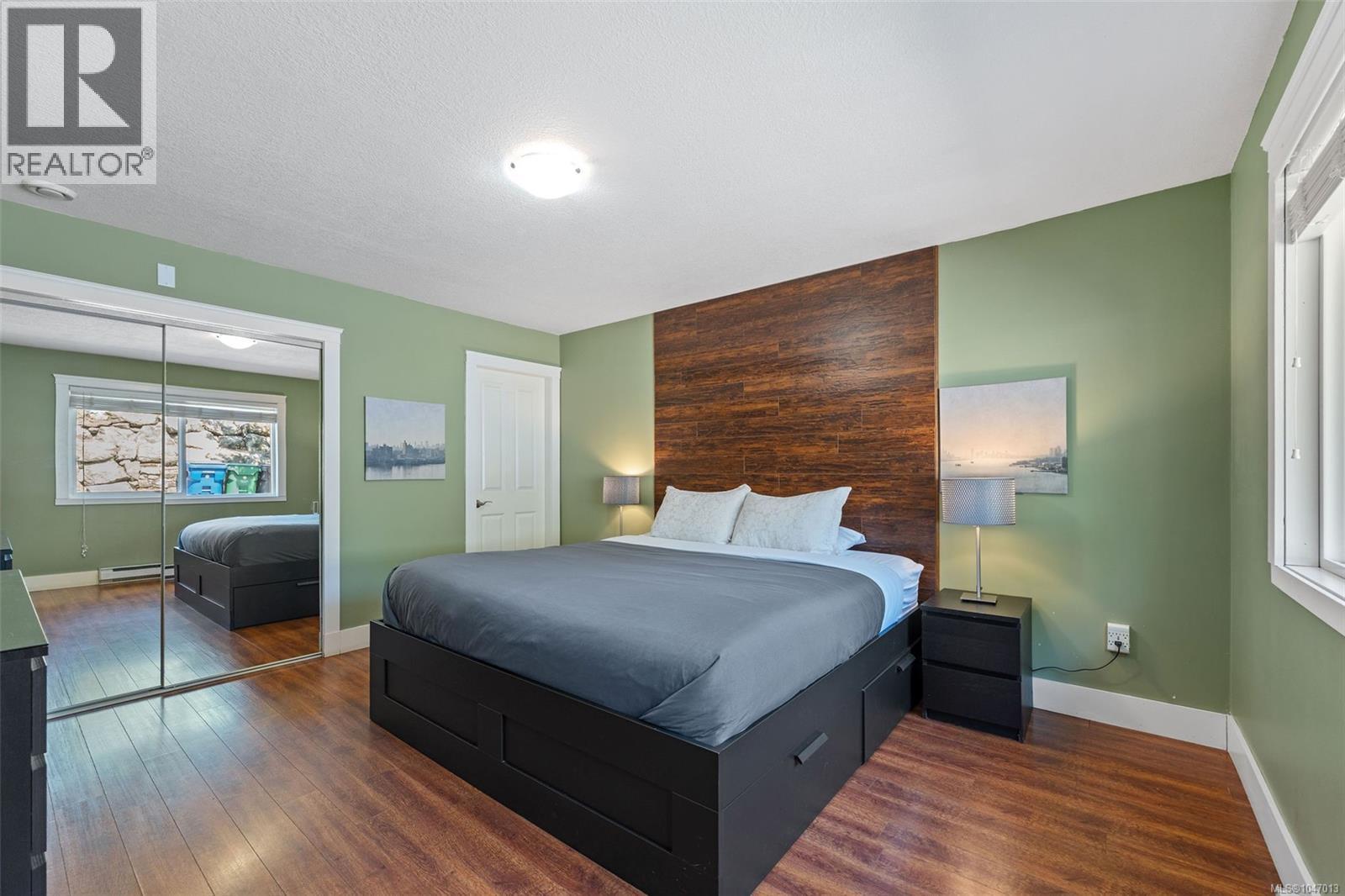 Large Master Bedroom with hardwood-finish flooring, accent wall with wood paneling, mirrored closet doors, recessed window, and an ensuite - 4105 Ross Rd, Nanaimo, BC - Indoor Photo Showing Bedroom