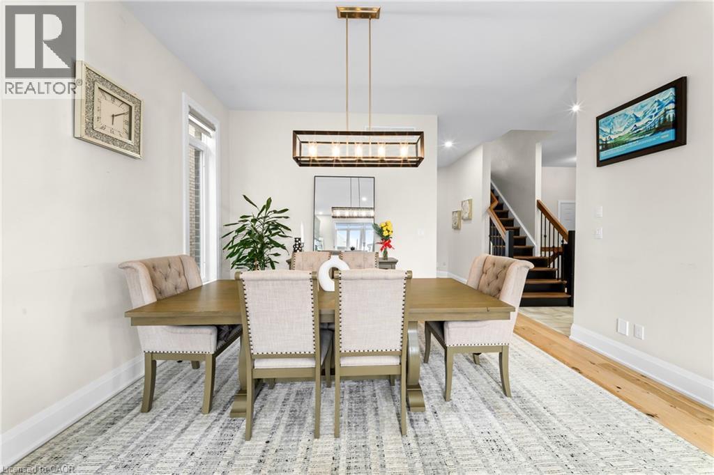 Formal dining area featuring a linear chandelier, light wood-finish flooring, and a stairway with dark wood treads and a wood railing - 130 Pondcliffe Drive, Kitchener, ON - Indoor Photo Showing Dining Room