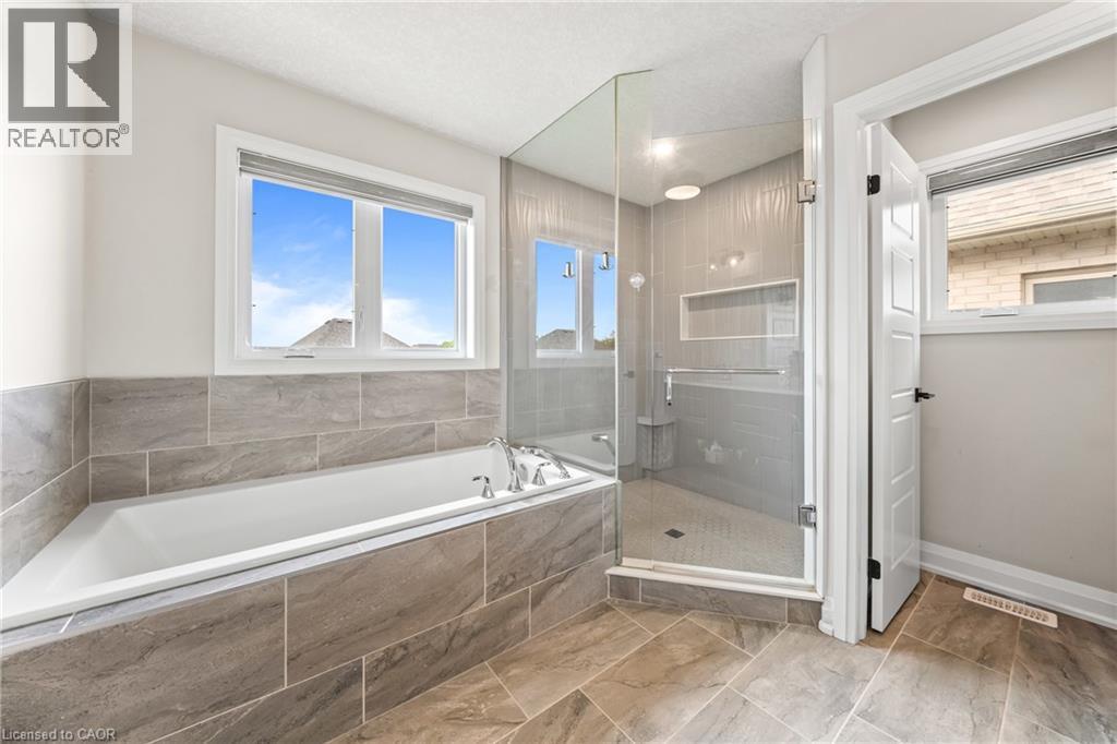 Spacious bathroom with a built-in soaking tub, framed windows, and large format tiled walls - 130 Pondcliffe Drive, Kitchener, ON - Indoor Photo Showing Bathroom