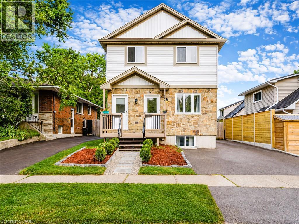 Two-story facade with stone and siding finishes, featuring a porch with railings, landscaped front beds, and a paved driveway - 67 Kinzie Avenue, Kitchener, ON - Outdoor With Facade