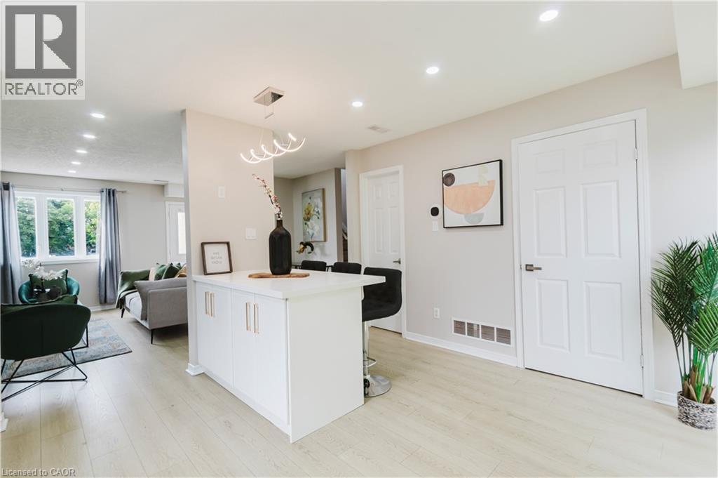 Light-toned wood-finish flooring throughout, white paneled doors, recessed ceiling lighting, and a white kitchen island with modern hardware - 67 Kinzie Avenue, Kitchener, ON - Indoor