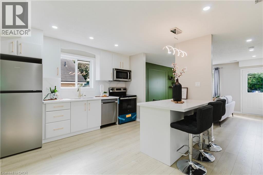 Bright kitchen featuring white cabinetry, stainless steel appliances, a white island with seating, and wood-finish flooring - 67 Kinzie Avenue, Kitchener, ON - Indoor Photo Showing Kitchen