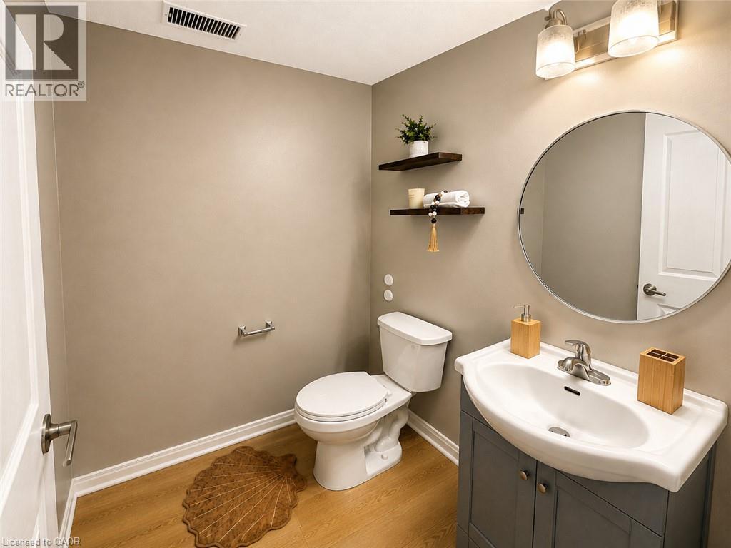 Wood-finish flooring, wall-mounted floating shelves, integrated sink, vanity with cabinet storage, and an oval mirror - 67 Kinzie Avenue, Kitchener, ON - Indoor Photo Showing Bathroom